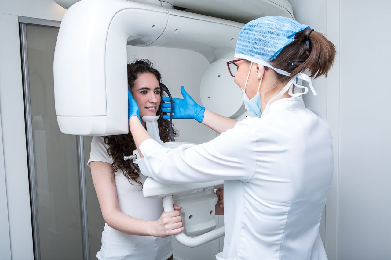 Dentista ajustando posição da cabeça da paciente na máquina para realizar radiografia panorâmica.