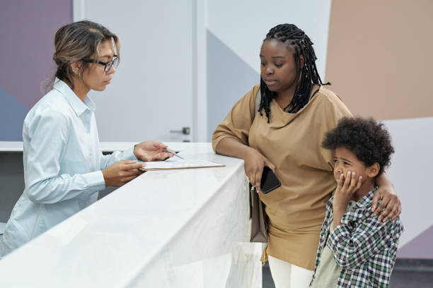 Recepcionista conversando com mãe de menino pequeno que está com dor de dente e segura a bochecha com expressão de dor.