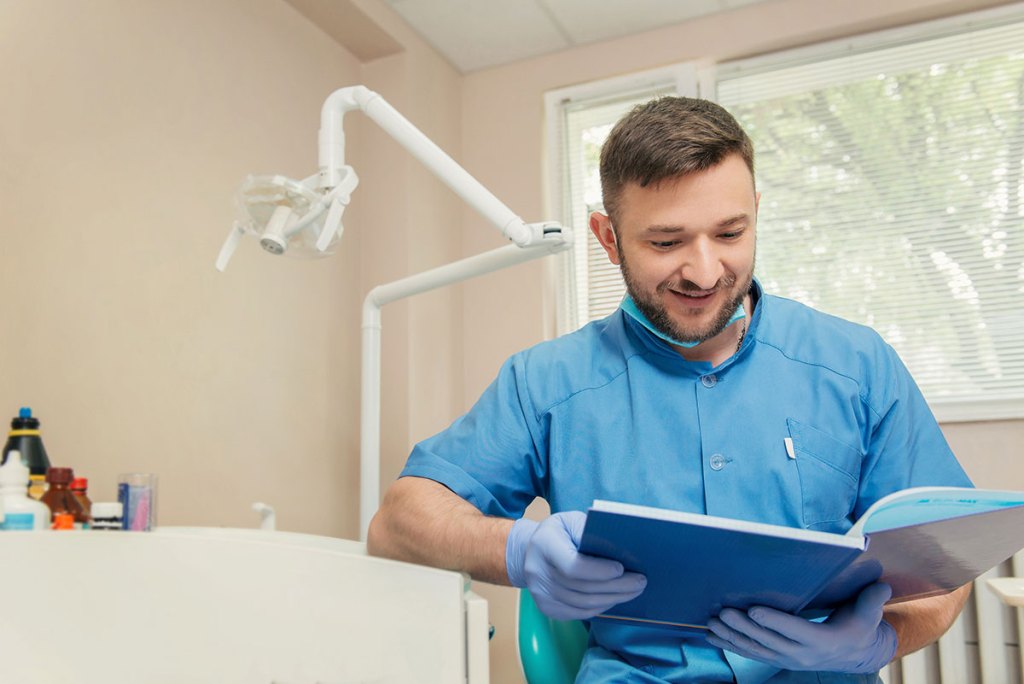 Dentista está sentado em seu consultório lendo um livro.