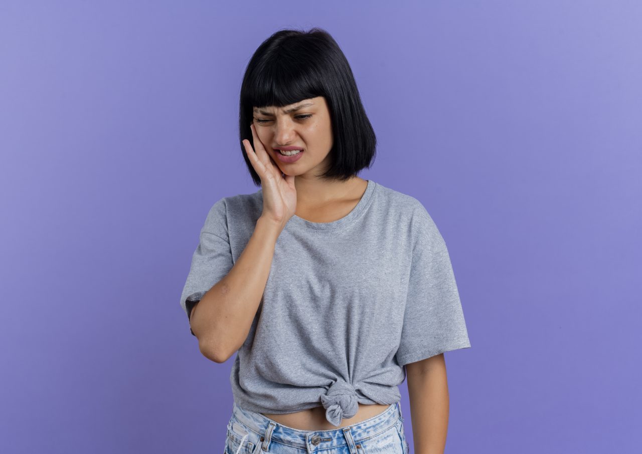 Jovem mulher está com dor de dente, ela aperta a bochecha.