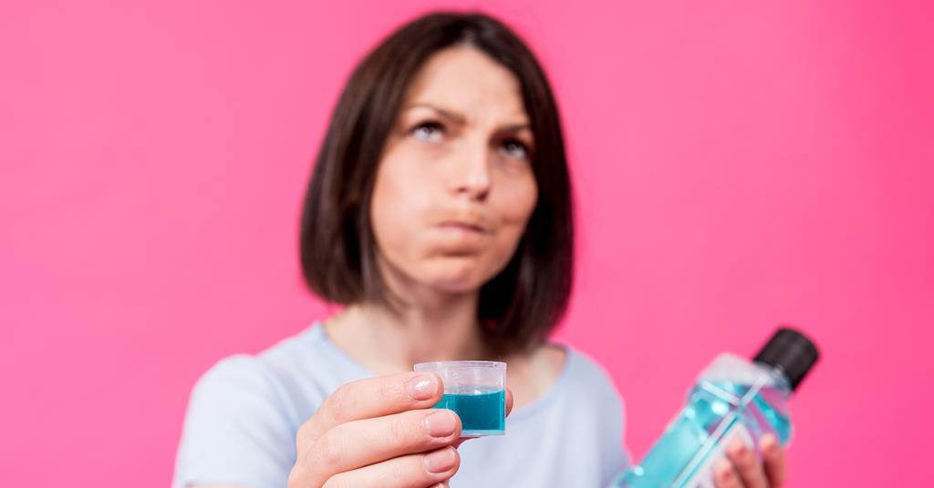 Mulher de cabelo no ombro está segurando um copinho com enxaguante bucal enquanto faz bochecho.