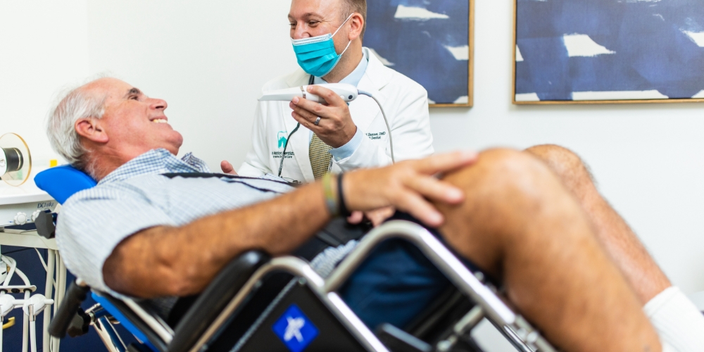 Dentista e paciente felizes durante consulta no hospital. O paciente é um senhor de cadeira de rodas.