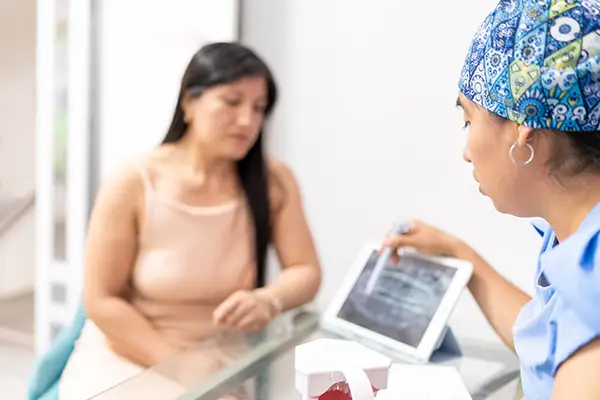 Dentista mostrando resultado de raio-x panorâmico para paciente que está sentada em sua frente no consultório.