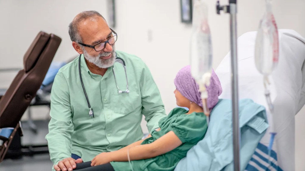 Médico falando com criança com leucemia que está recebendo soro no hospital.