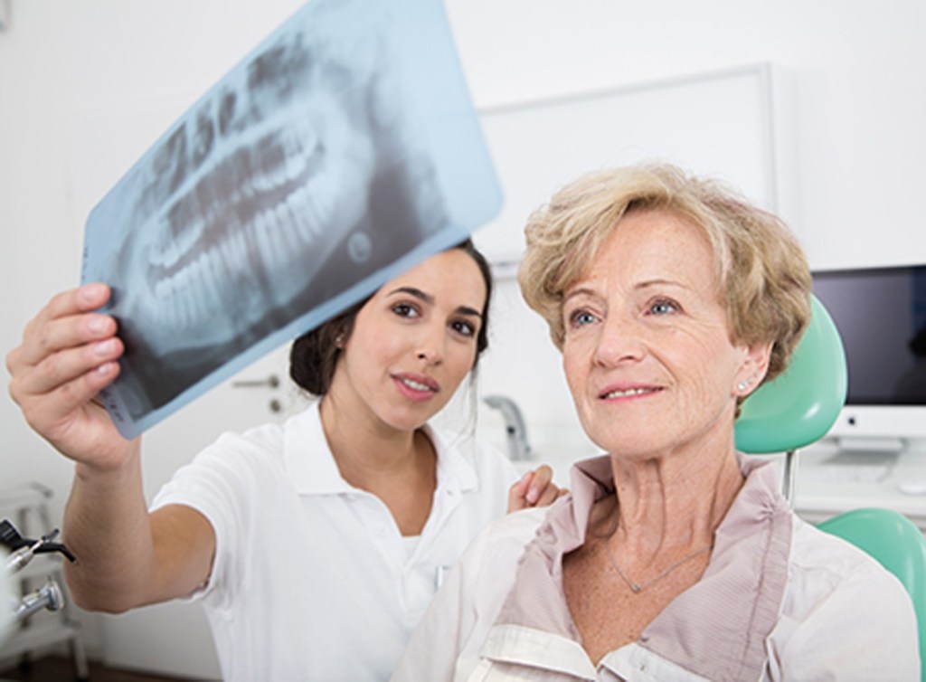 Dentista mostrando resultado de panorâmica para paciente idosa em seu consultório.