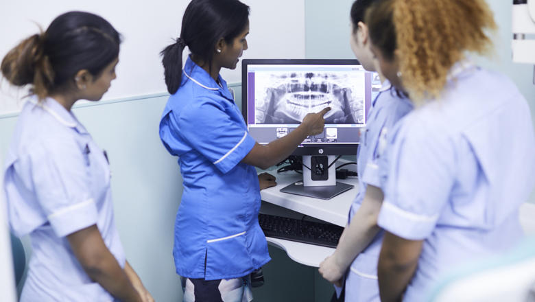 Dentista mostrando para outras um ponto no raio-x no computador.