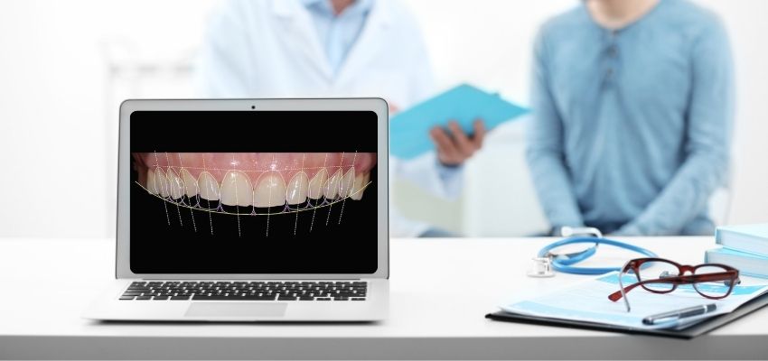 Dentistas ao fundo conversando e segurando prancheta. Na frente tem um notebook aberto com planejamento digital do sorriso.