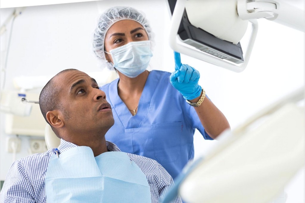 Dentista mostra algo na tela para o paciente.