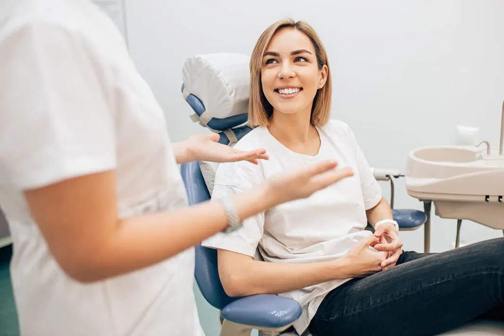 Dentista explicando procedimento para paciente que sorri atenciosa.
