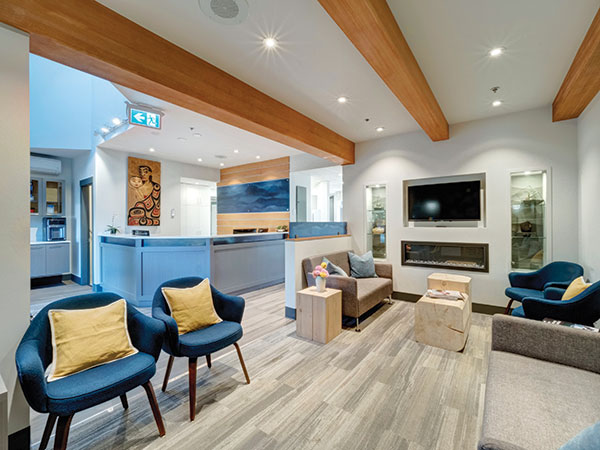 Sala de espera de clínica odontológica aconchegante. Com cores azuis e marfim, tem poltronas e sofás com travesseiros.