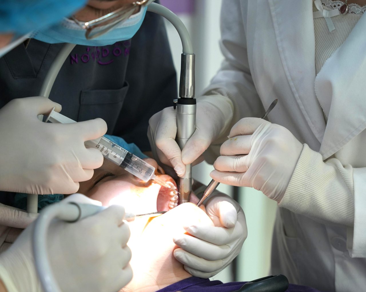 Dentista e assistentes tratando dentes de paciente.