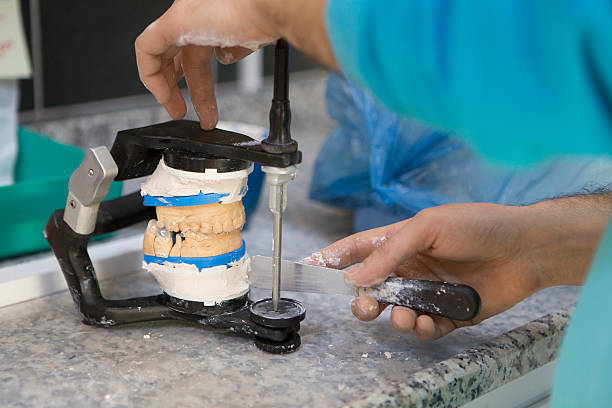 Colocou molde de prótese no articulador e está ajustando a massa do gesso com espátula.