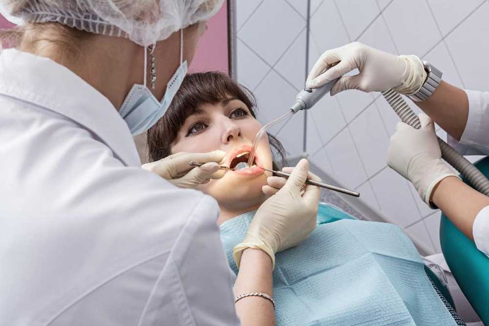 Dentista e assistente estão realizando tratamento dentário em paciente.