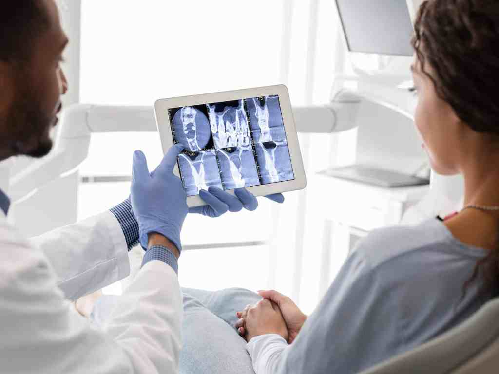 Dentista mostrando raio-x para paciente em tablet.