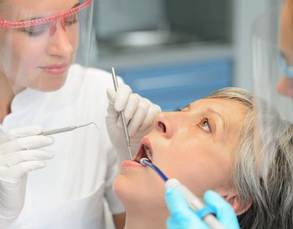 Dentista realizando limpeza em boca de paciente.