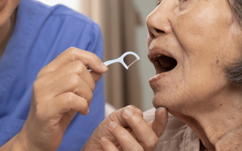 Dentista vai passar fio dental forquilha em idosa.