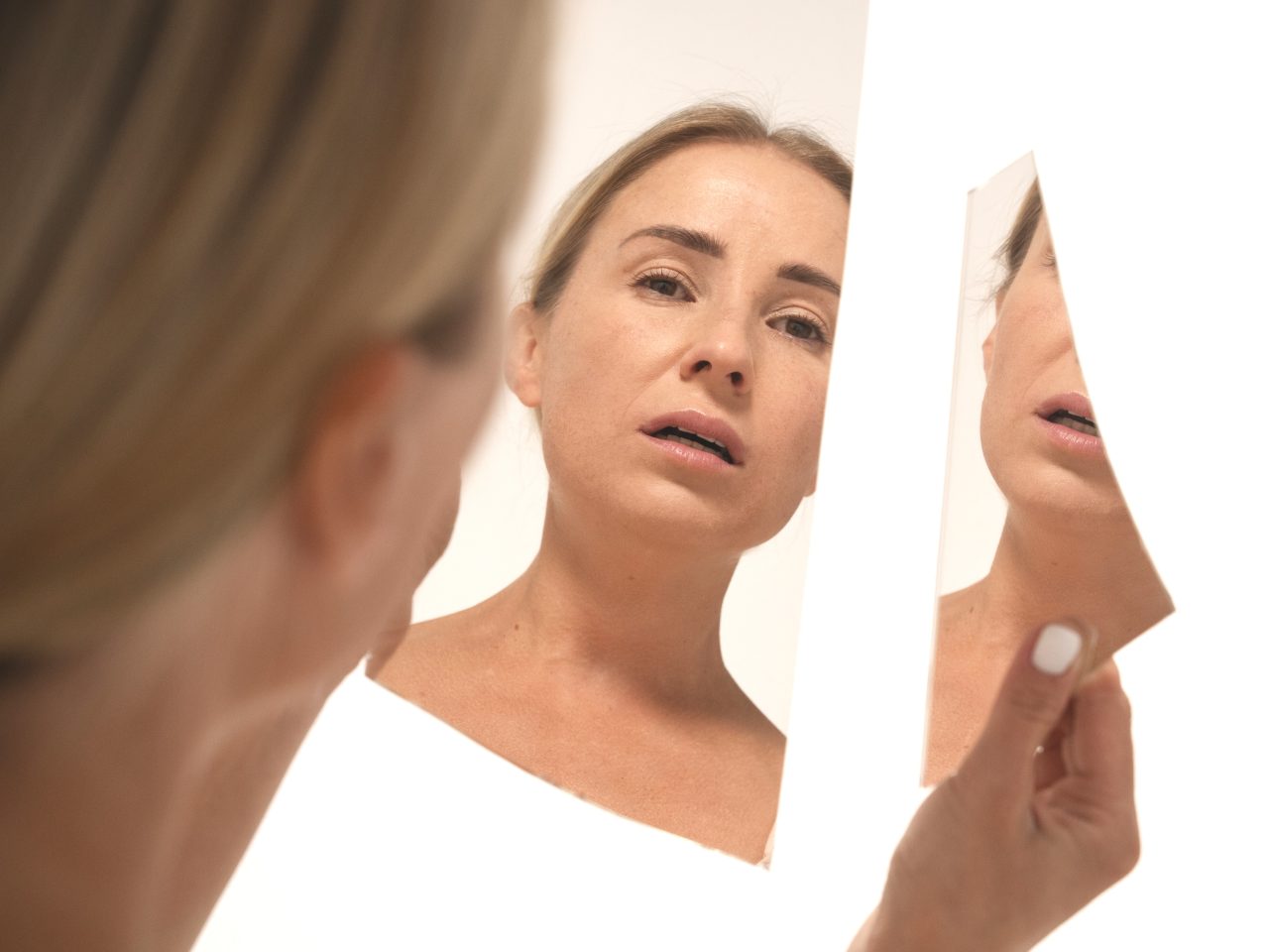 Mulher se olhando em dois pedaços de espelho quebrado.