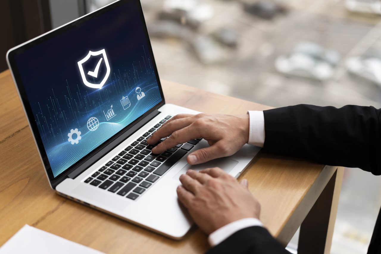 Homem está mexendo em notebook que possui símbolo de segurança de dados.