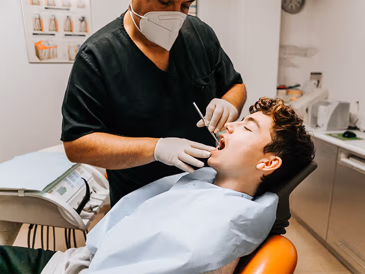 Dentista realizando limpeza em dente de paciente jovem garoto.