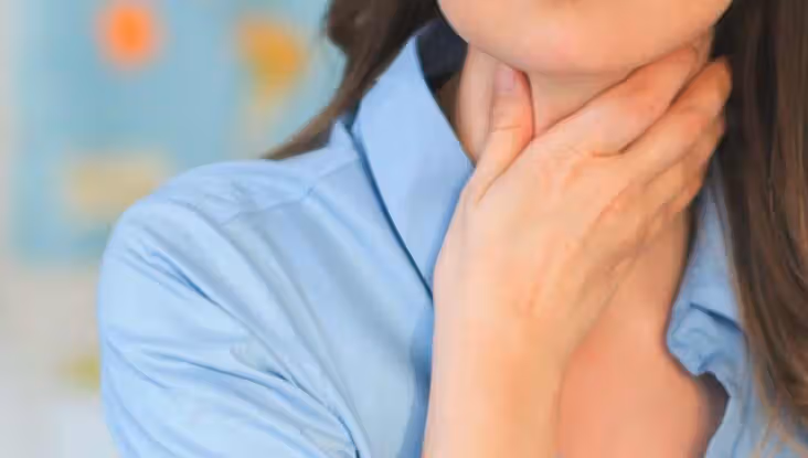 Mulher sente dor de garganta e coloca a mão no pescoço.