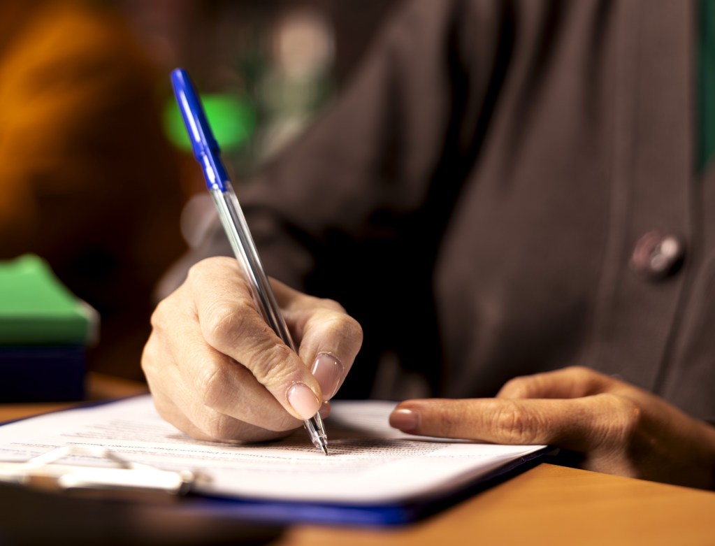 Mulher está fazendo anotações em documento em prancheta.
