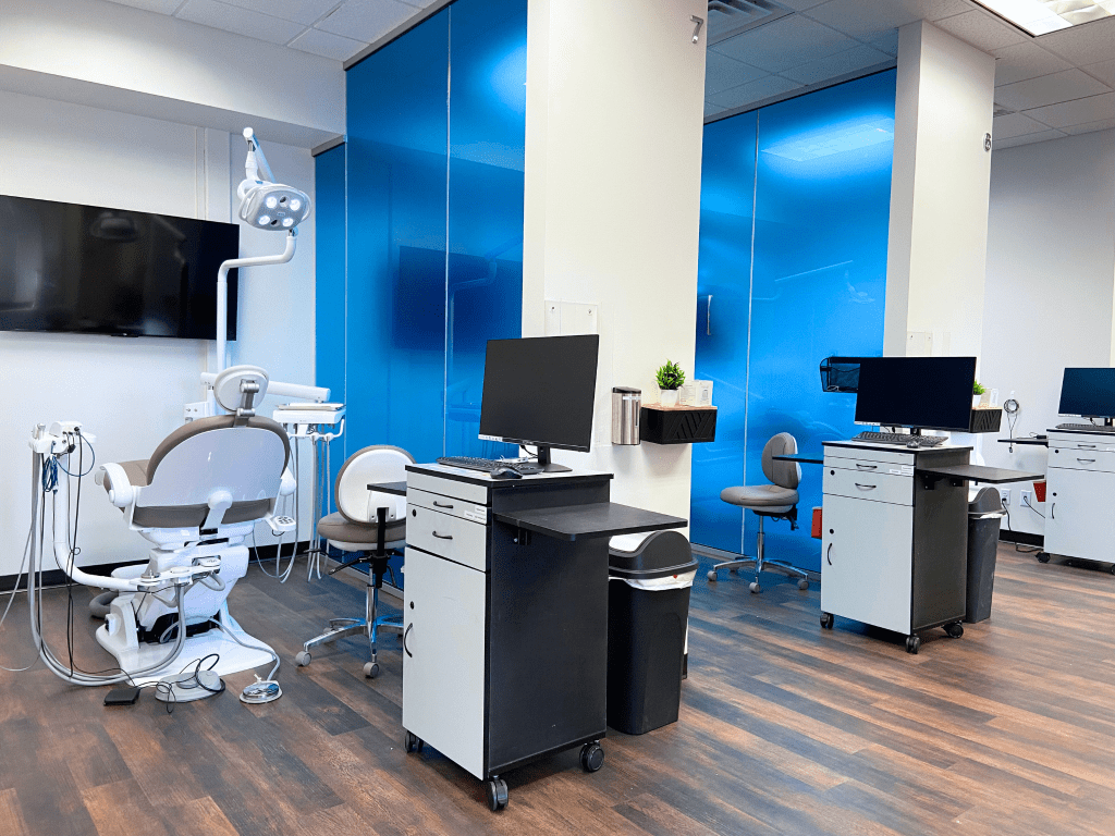 Imagem de dentro de uma clínica odontológica com vários consultórios abertos lado a lado separados por uma parede de vidro azul.