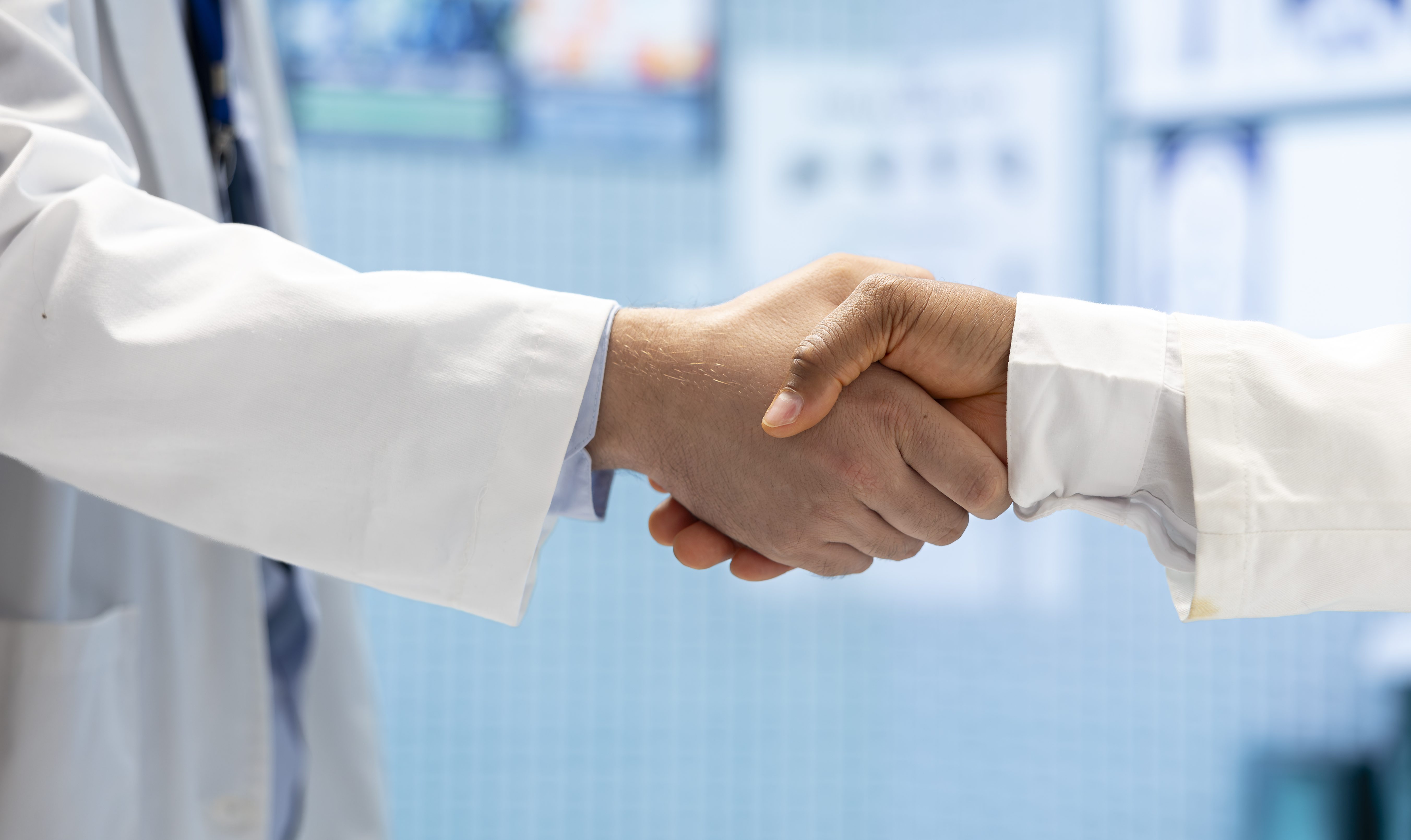 Profissionais com jaleco dando um aperto de mão.