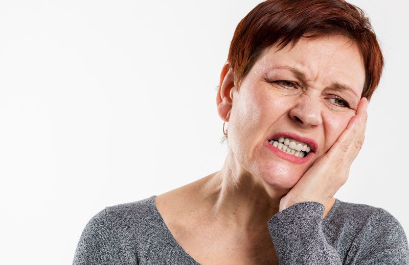 Senhora está com dor no dente, apoia a mão na face.