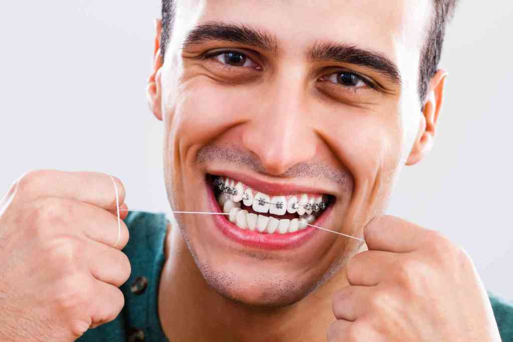 Homem com aparelho passa fio dental