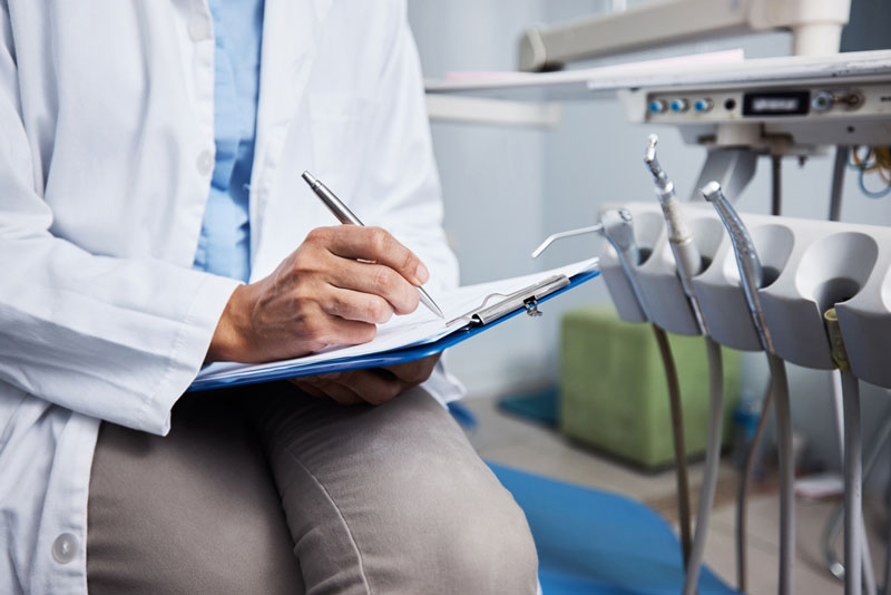 Dentista sentado em consultório fazendo anotações em sua prancheta,