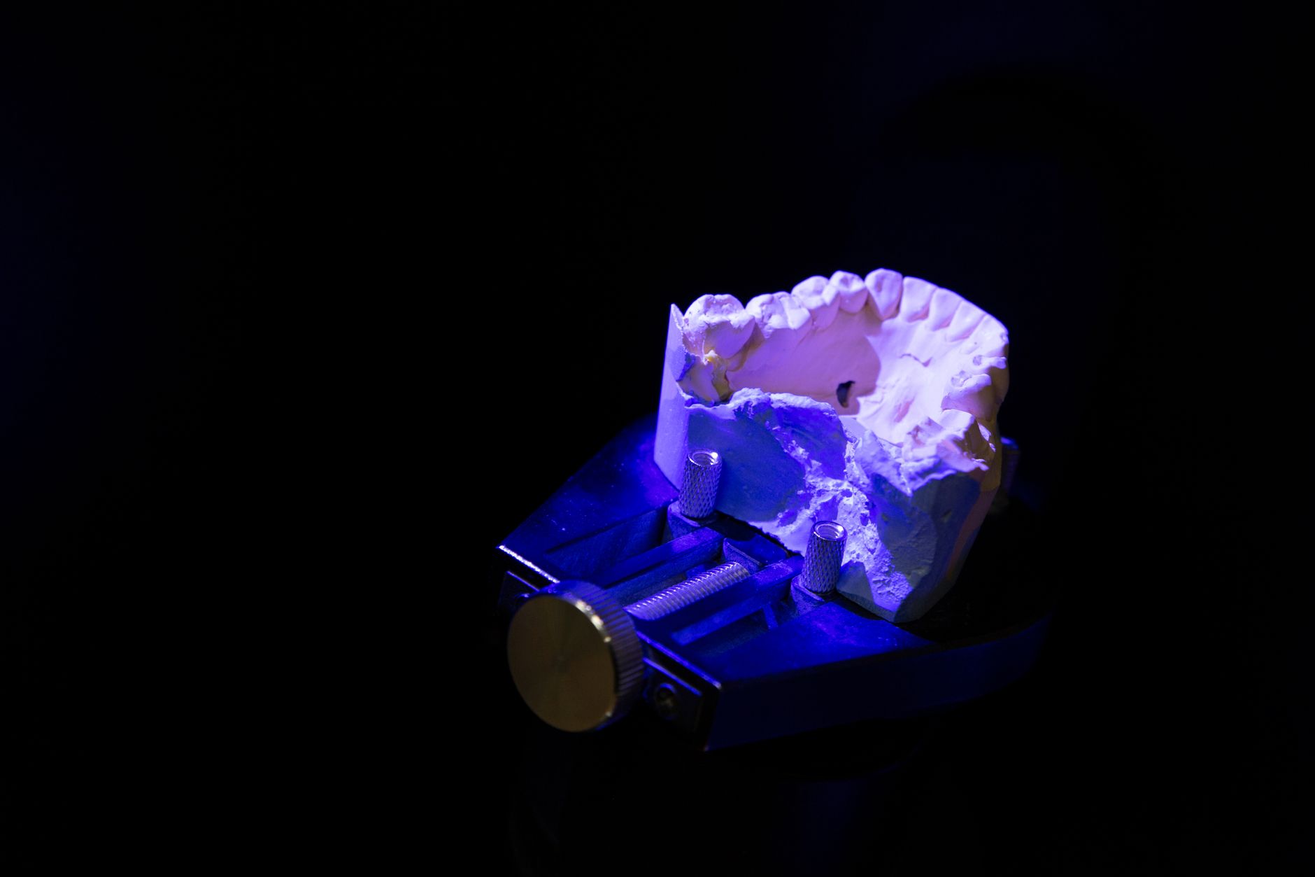 From above of white dental impression for creating denture placed on table in darkness illuminated by blue light against black background